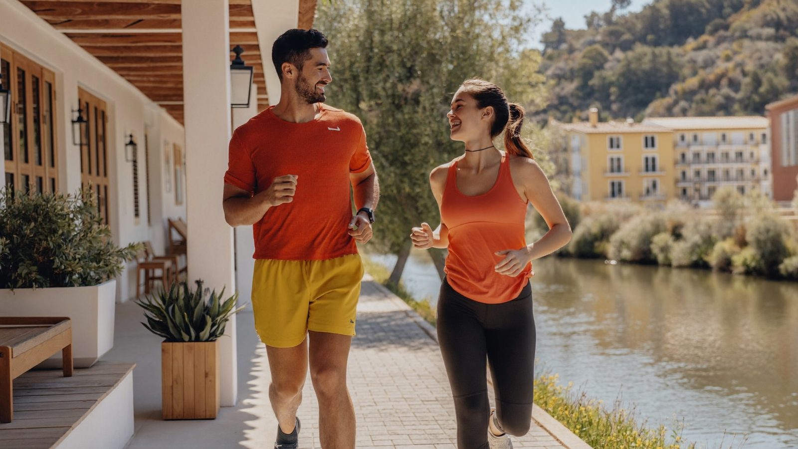 Dos personas corriendo a ritmo suave por un parque junto al río al amanecer